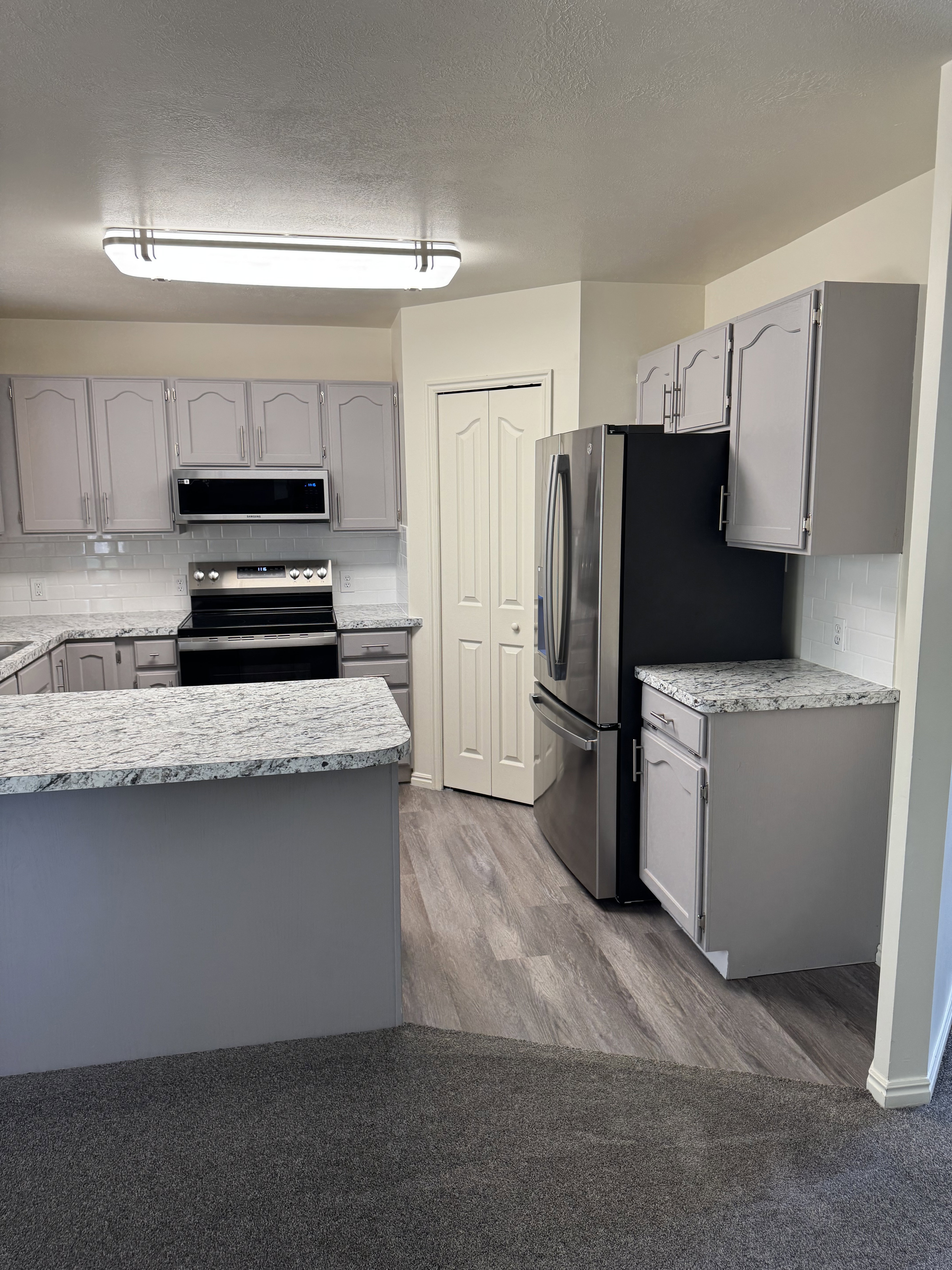 Kitchen featuring granite-style countertops, grey cabinetry, stainless steel appliances, and wood-finish flooring