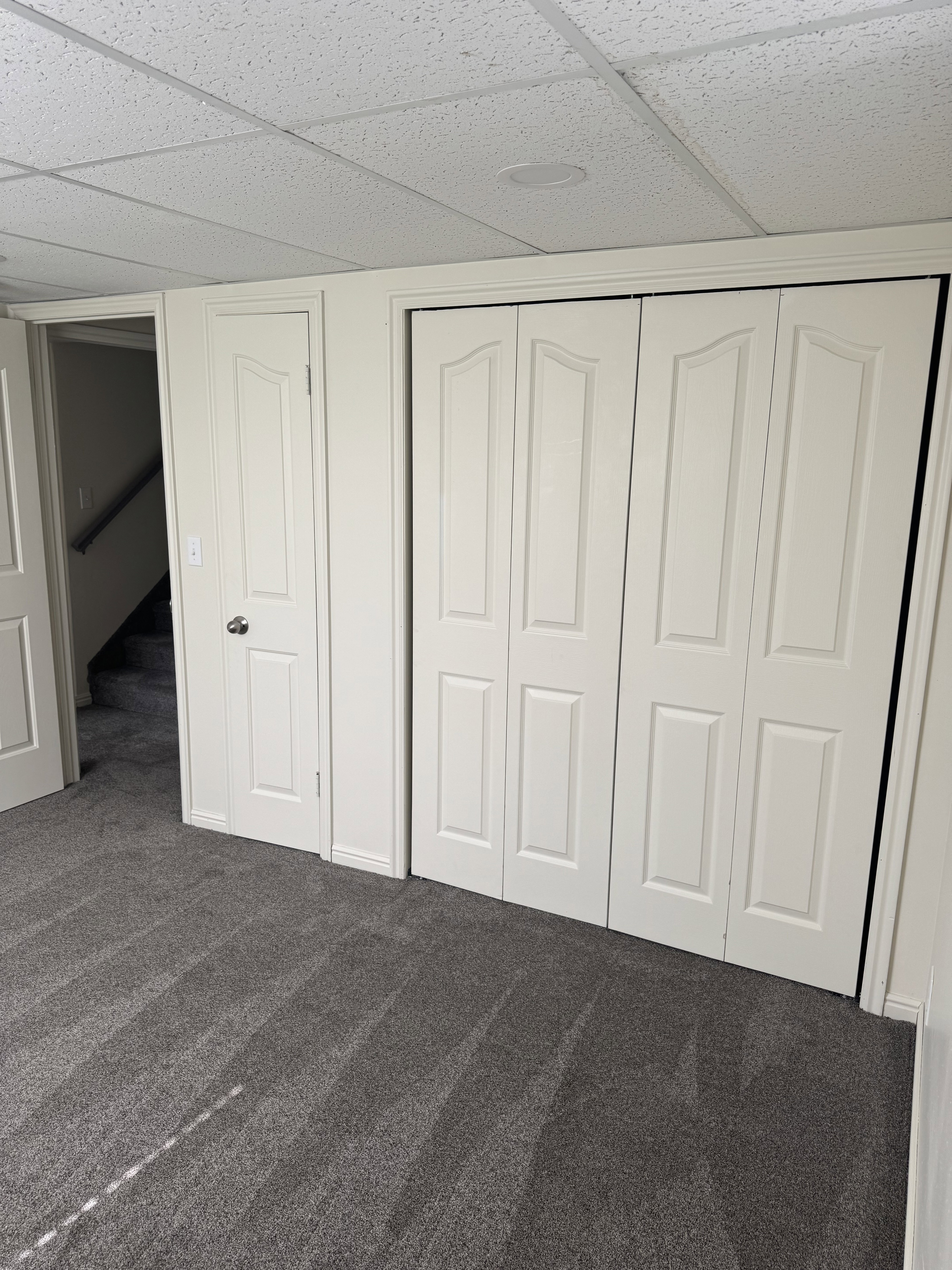 Recessed lighting illuminating a plush gray carpeted room with white bi-fold closet doors and a white paneled door