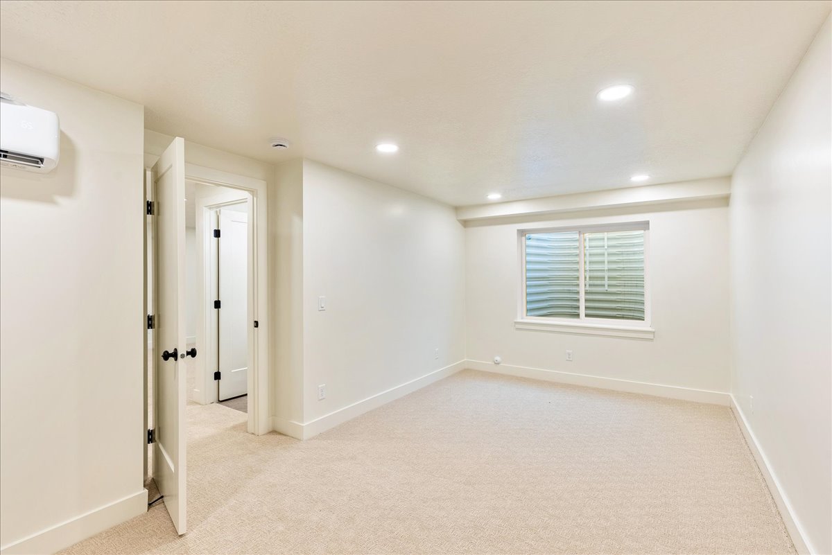 Spacious room featuring neutral carpet flooring, recessed lighting, a horizontal sliding window, a wall-mounted mini-split unit, and a paneled interior door with matte black hardware