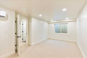 Spacious room featuring neutral carpet flooring, recessed lighting, a horizontal sliding window, a wall-mounted mini-split unit, and a paneled interior door with matte black hardware