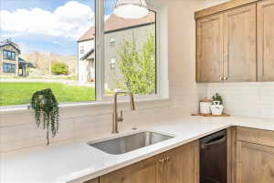 Kitchen featuring a stainless steel sink with a gooseneck faucet, light wood-finish cabinetry, a built-in dishwasher, white countertops, and a white subway tile backsplash