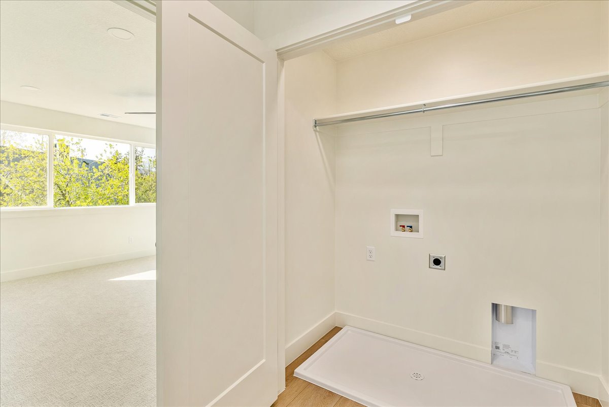 Dedicated laundry alcove with a built-in hanging rod, utility hookups, and a drain pan
