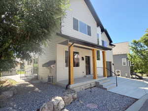 Modern two-story residence featuring light-colored siding, a covered front porch with wood columns, dark trim, and a gravel front yard with rock landscaping