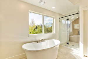 Spacious bathroom featuring a freestanding soaking tub with brass fixtures, a walk-in glass-enclosed shower with a built-in bench, and light-toned tile flooring