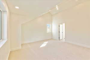 Spacious room featuring vaulted ceilings, recessed lighting, neutral wall tones, plush carpeting, and multiple windows