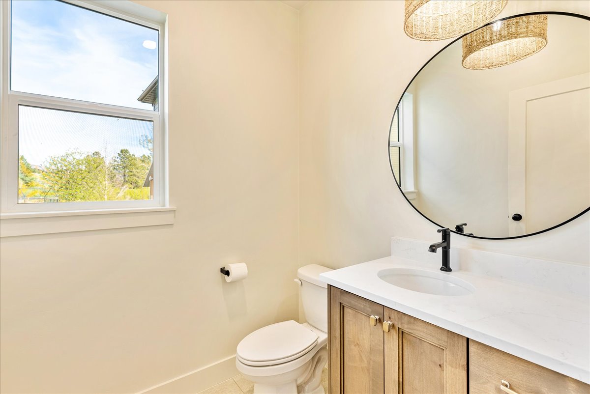 Bathroom featuring a wood-finish vanity with a white countertop, an oval mirror, and a white toilet