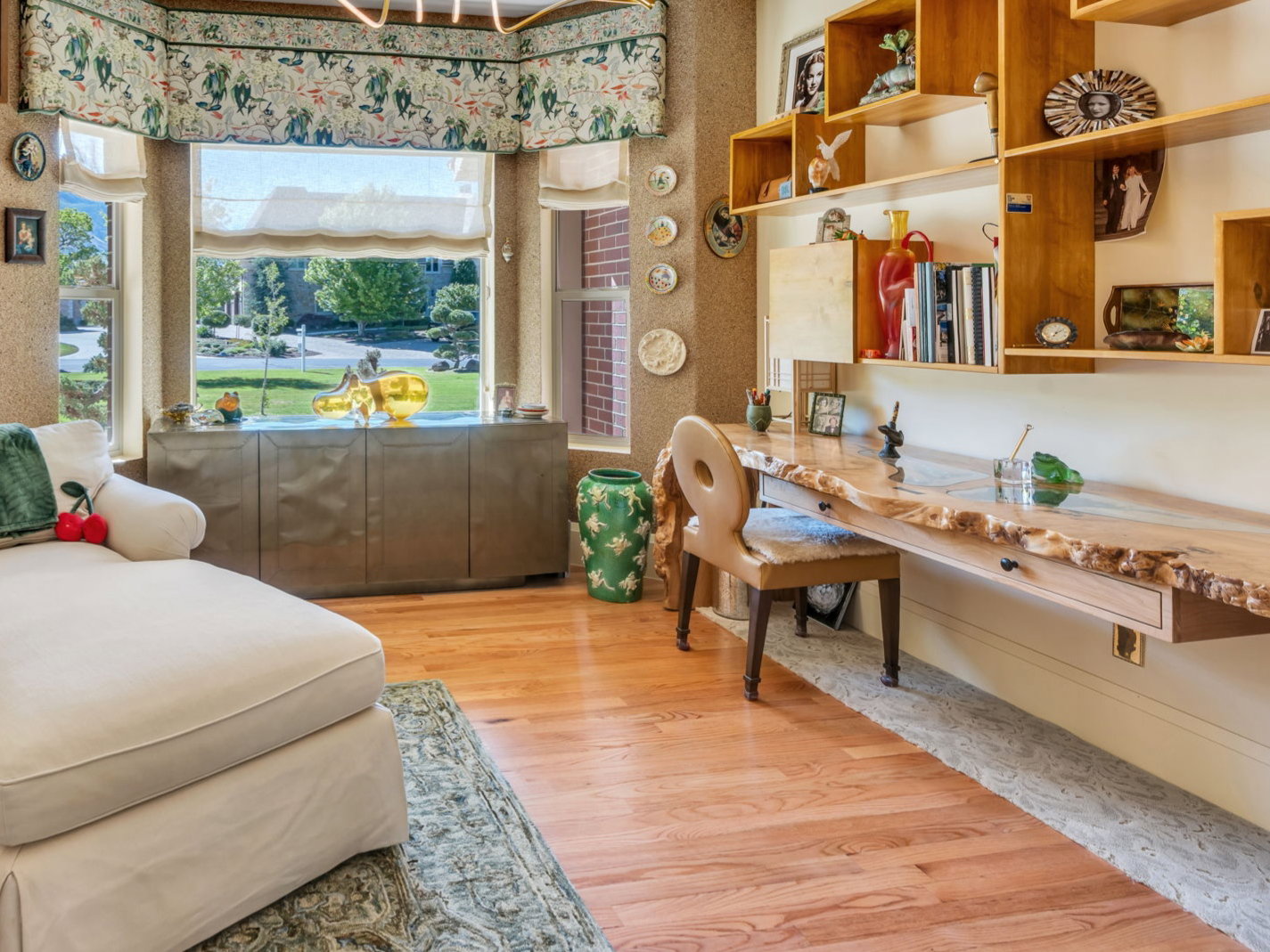 Room featuring wood-finish flooring, a prominent bay window with custom valance, a built-in live edge wood desk with integrated shelving, and a modern linear chandelier