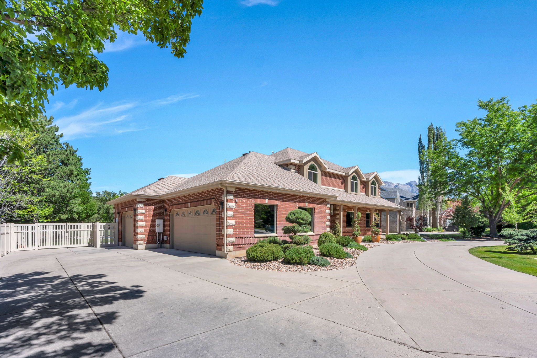 Brick exterior residence with a multi-car garage, circular driveway, arched dormer windows, and established landscaping