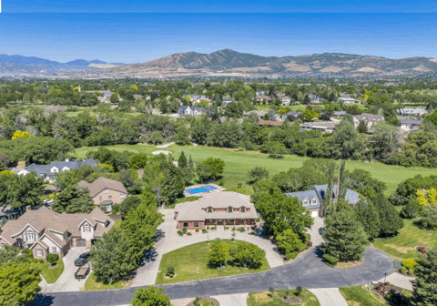 Aerial perspective highlighting a residential property with a brick exterior, a circular driveway, and mature landscaping