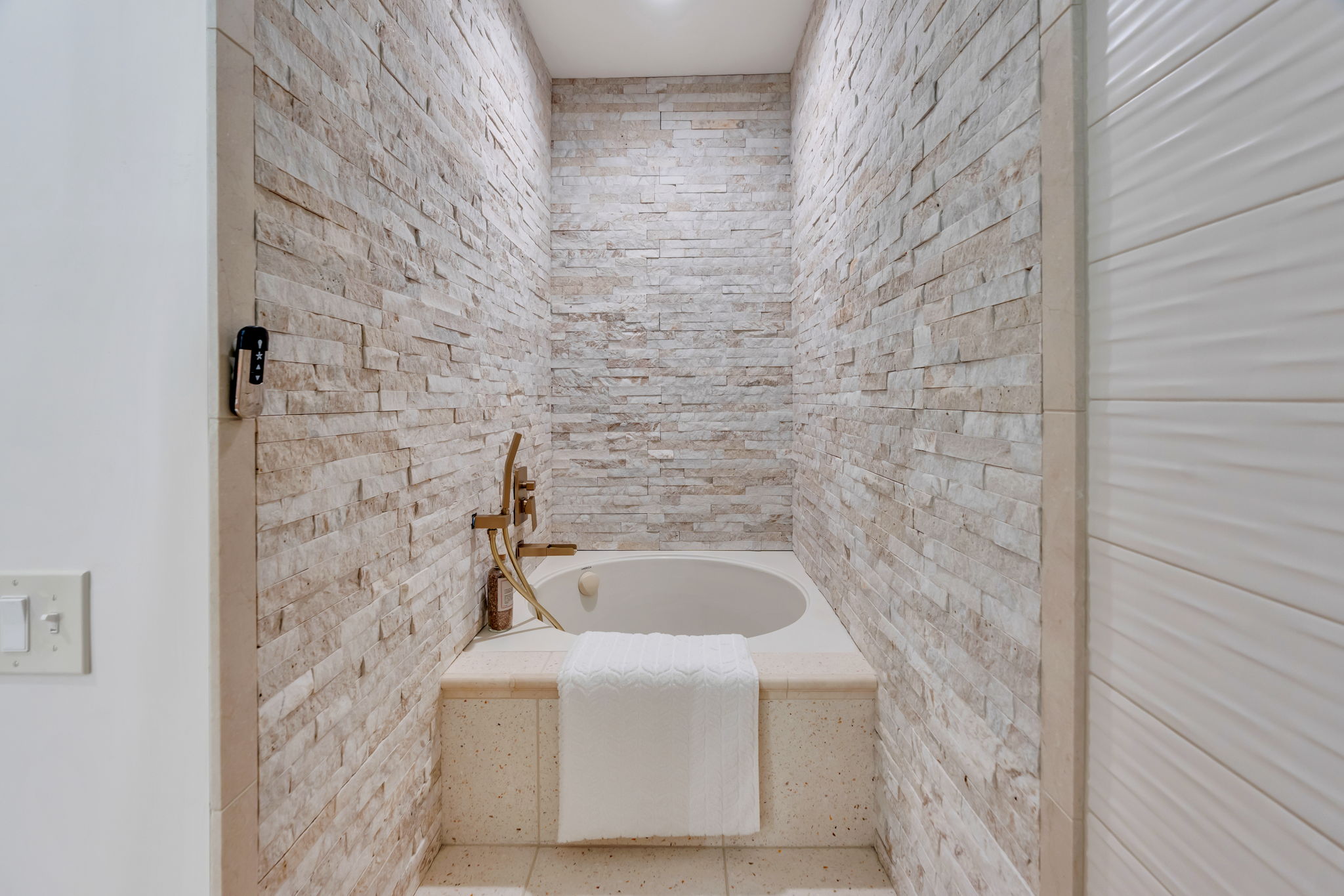Recessed soaking tub with surrounding stone-finish decking, set within a textured stacked stone accent wall