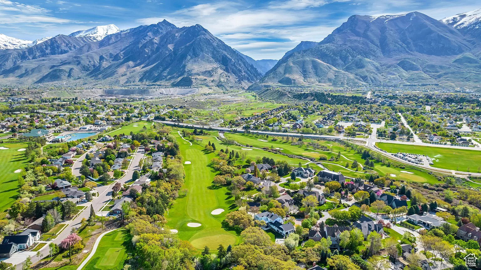 Aerial perspective showcasing a residential area with lush green landscapes, a golf course, and a prominent mountainous backdrop