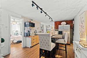 Kitchenette featuring wood-finish flooring, a stainless steel refrigerator, dark track lighting, a built-in microwave, and exposed brick accents