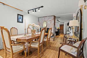 Hardwood flooring extends throughout this dining area, featuring a track lighting system and a partial exposed brick wall