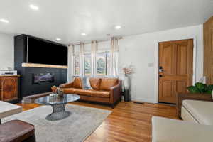 Living area featuring wood-finish flooring, recessed lighting, and a prominent fireplace with a dark shiplap surround and a light-toned wood mantel