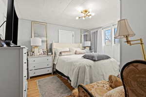 Bedroom featuring wood-finish flooring, a contemporary ceiling light fixture, multiple windows with drapes, a built-in closet door, and geometric patterned wallpaper