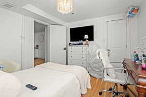 Bedroom featuring wood-finish flooring, a decorative chandelier, white walls, and a white paneled door