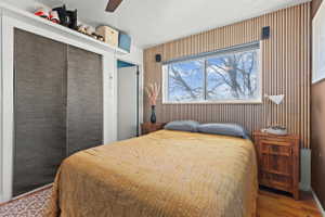 Bedroom featuring a wood-panel accent wall, overhead ceiling fan, and wood-finish flooring