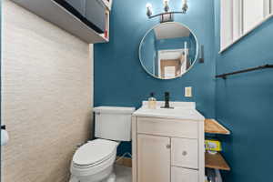 Compact powder room featuring a white vanity with integrated sink, black matte faucet, and circular mirror