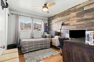 Room featuring wood-finish flooring, a decorative accent wall with horizontal paneling, and a ceiling fan with integrated lighting