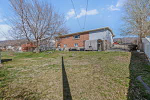Expansive sloped yard featuring a combination of brick and siding exterior, a white vinyl fence, and a mature tree