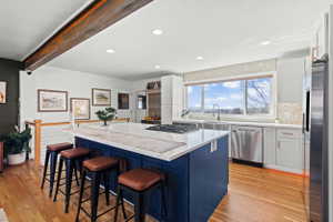 Open-concept kitchen featuring an oversized island with a built-in gas cooktop, stainless steel appliances, light-toned cabinetry, and wood-finish flooring