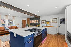 Kitchen island featuring a gas range, white countertop, and blue cabinetry