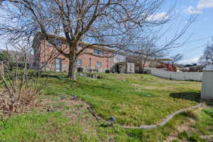 Spacious backyard featuring a large tree, brick exterior, and a white fence