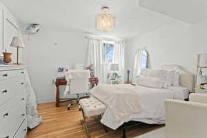 Room featuring wood-finish flooring, a crystal chandelier, and a window with white curtains