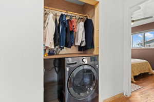 Built-in laundry closet featuring a front-load washer, wood-finish shelving, and a hanging rod