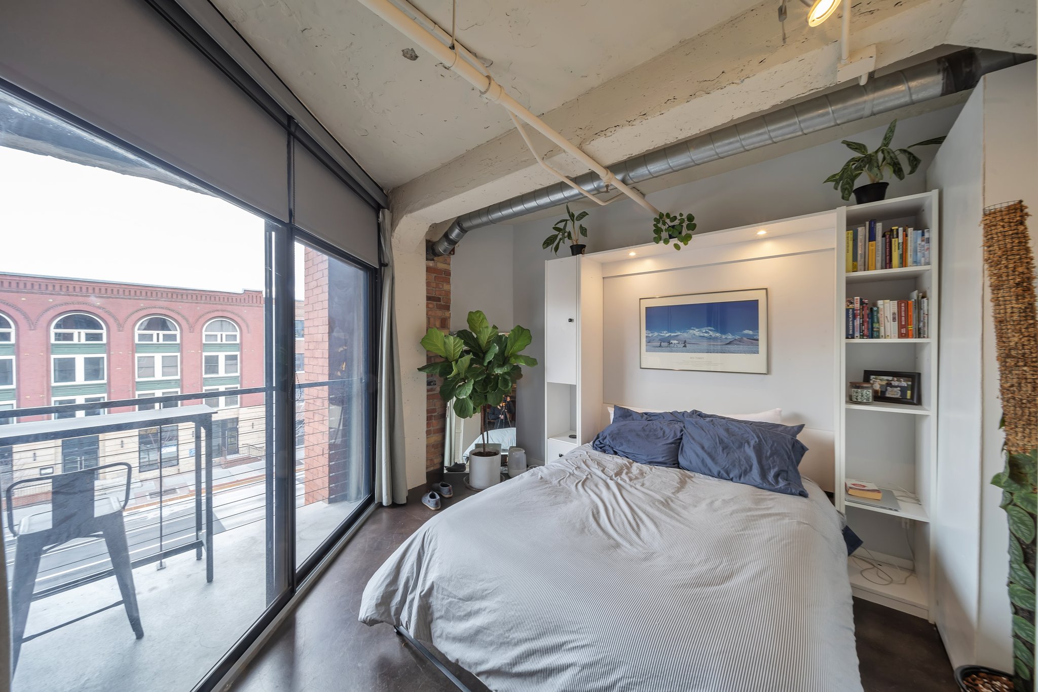 Bedroom featuring exposed brick accents, dark wood-finish flooring, and a floor-to-ceiling glass door opening to a private balcony