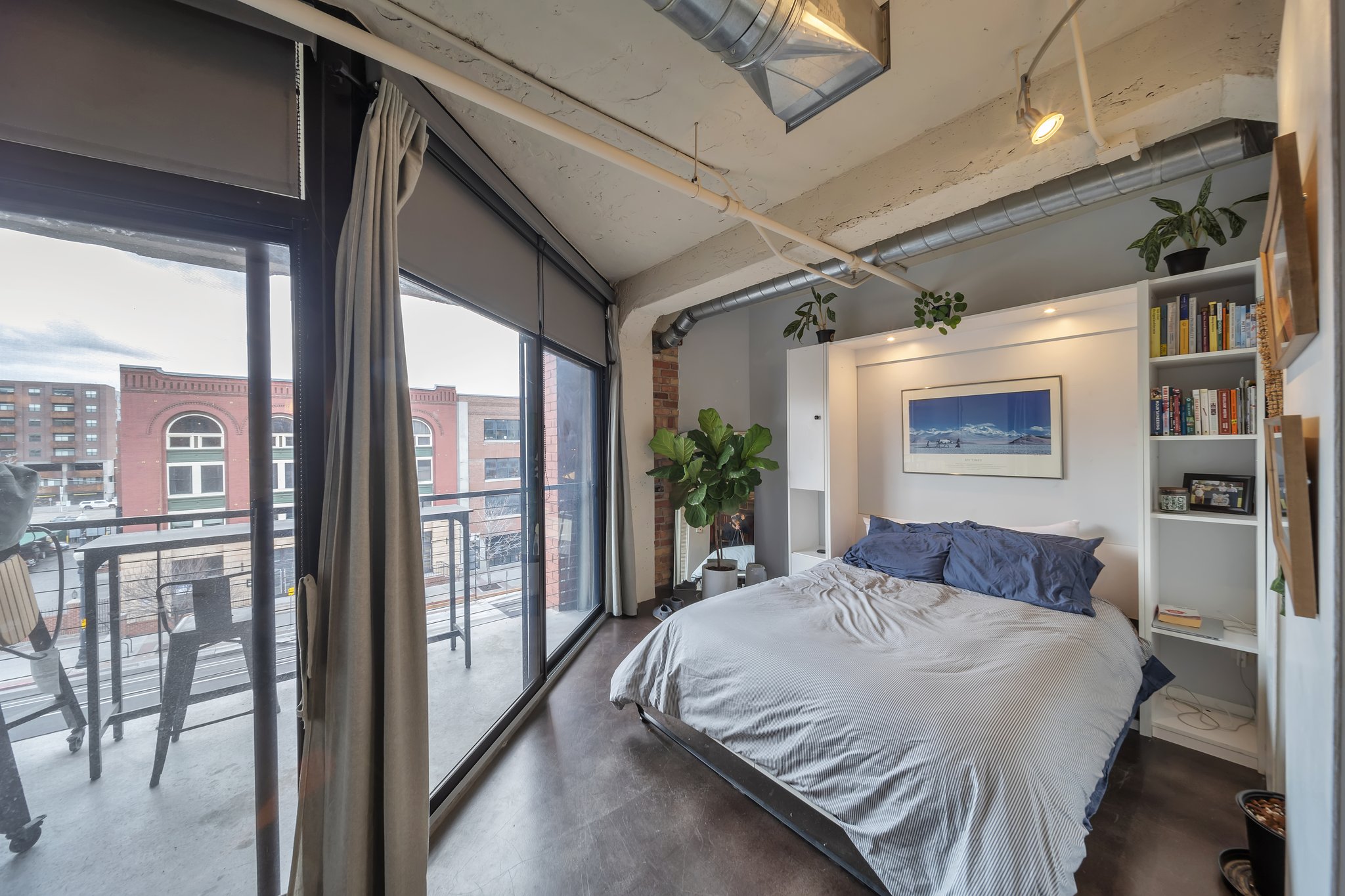 Industrial-style bedroom featuring exposed ductwork, concrete-finish ceilings, and sliding glass doors leading to a balcony