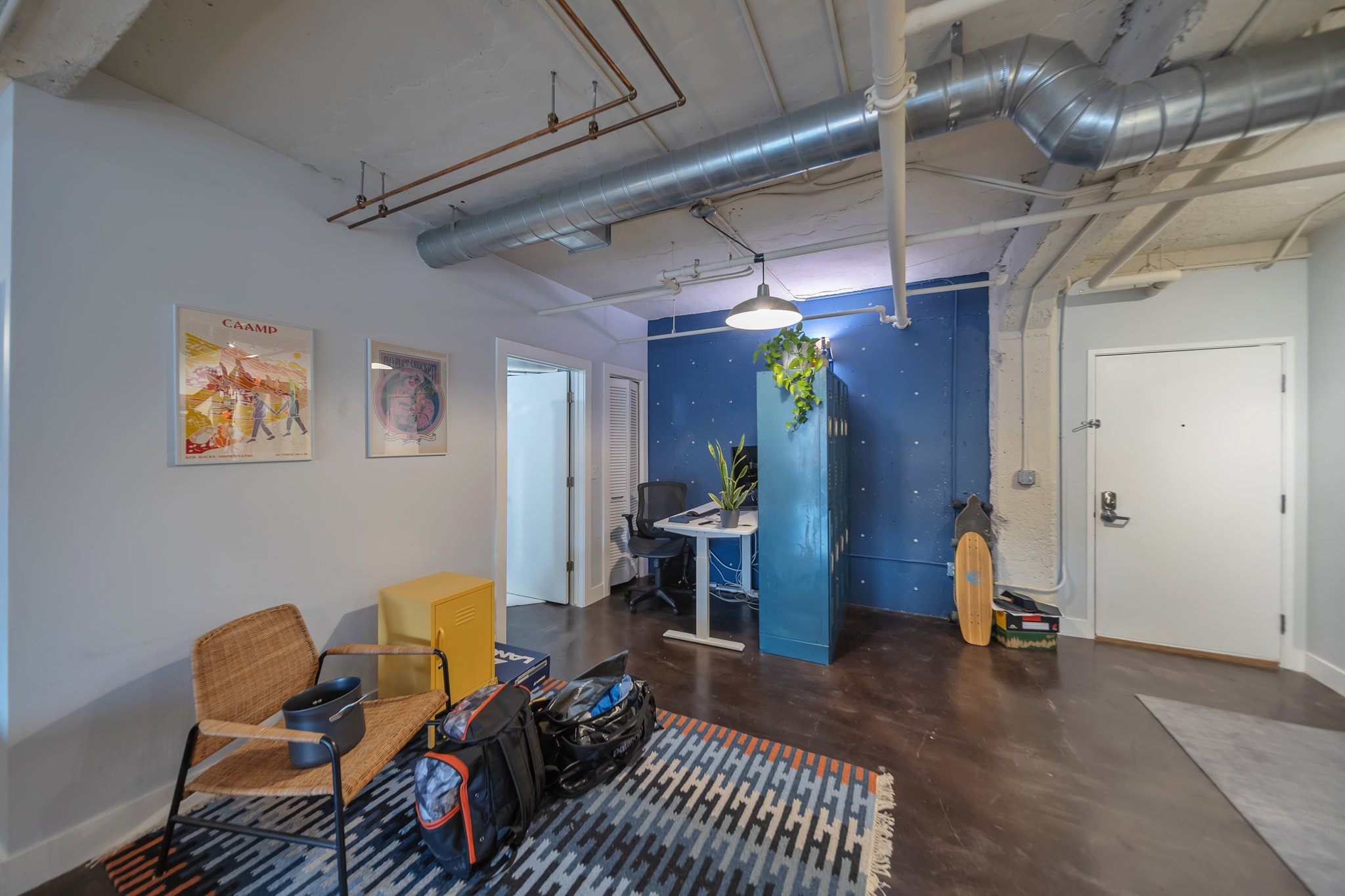 Open-concept interior featuring exposed ductwork and ceiling pipes, concrete ceilings, dark wood-finish flooring, and a blue accent wall