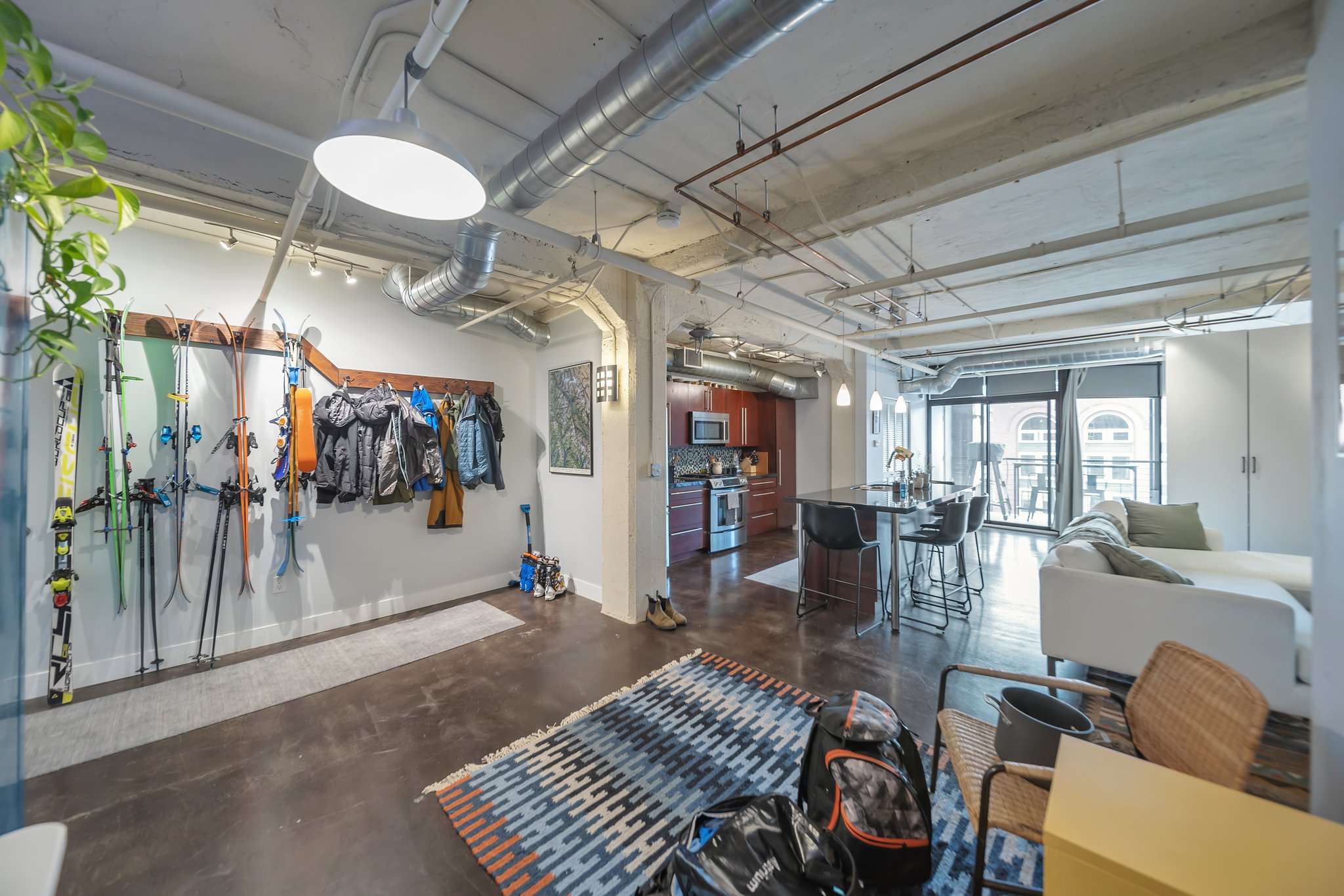 Open-concept living area featuring exposed ductwork, dark-finish flooring, a kitchen with dark cabinetry and stainless steel appliances, and glass doors opening to an exterior space