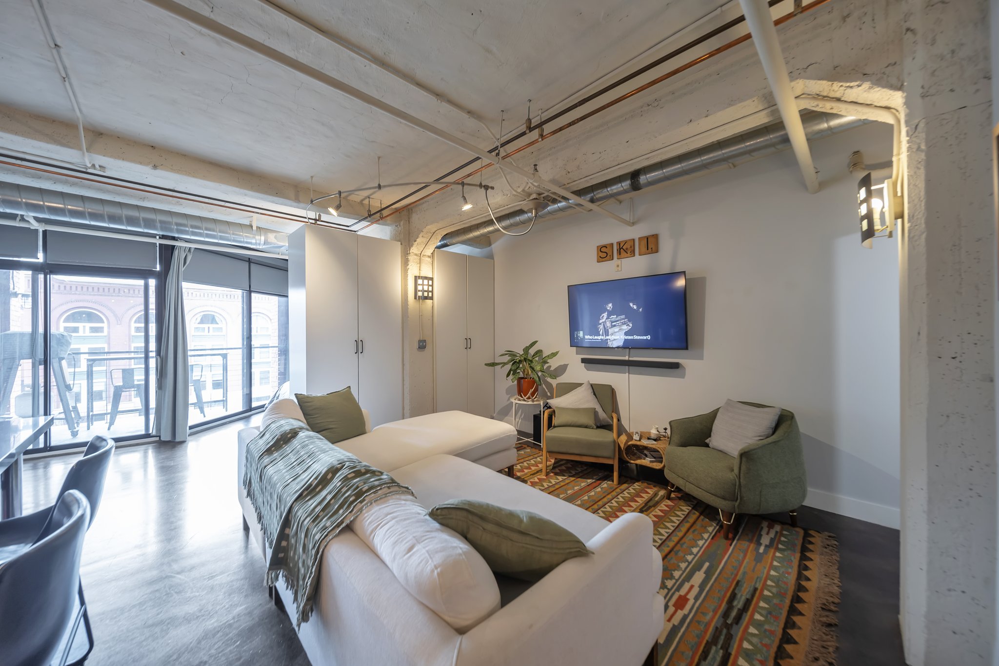 Expansive living space featuring exposed concrete ceilings and columns, industrial-style track lighting, a full wall of built-in storage, and wood-finish flooring