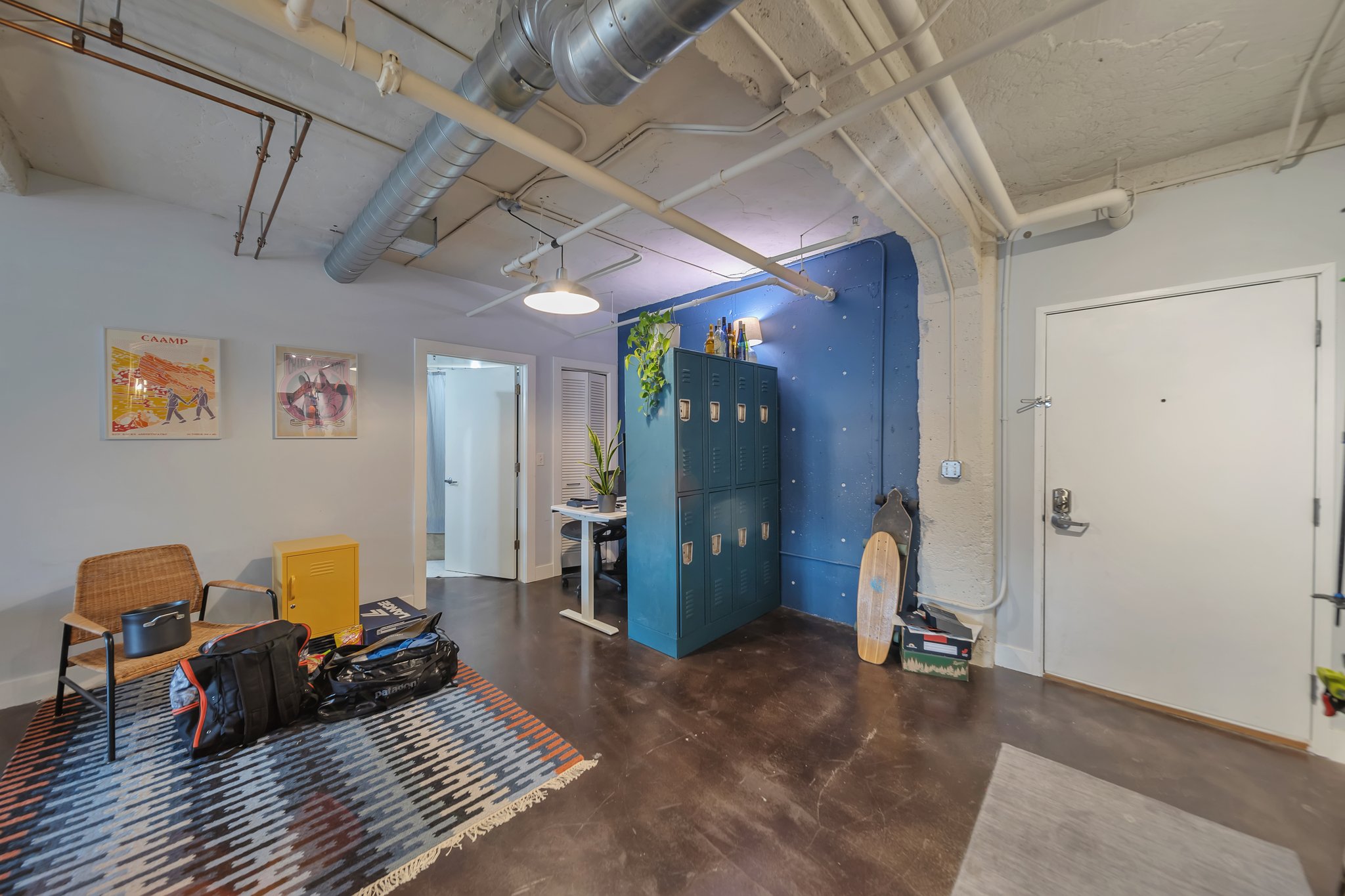Interior space featuring exposed ductwork and conduit, concrete ceilings, dark-finish flooring, and a vibrant blue accent wall with integrated shelving