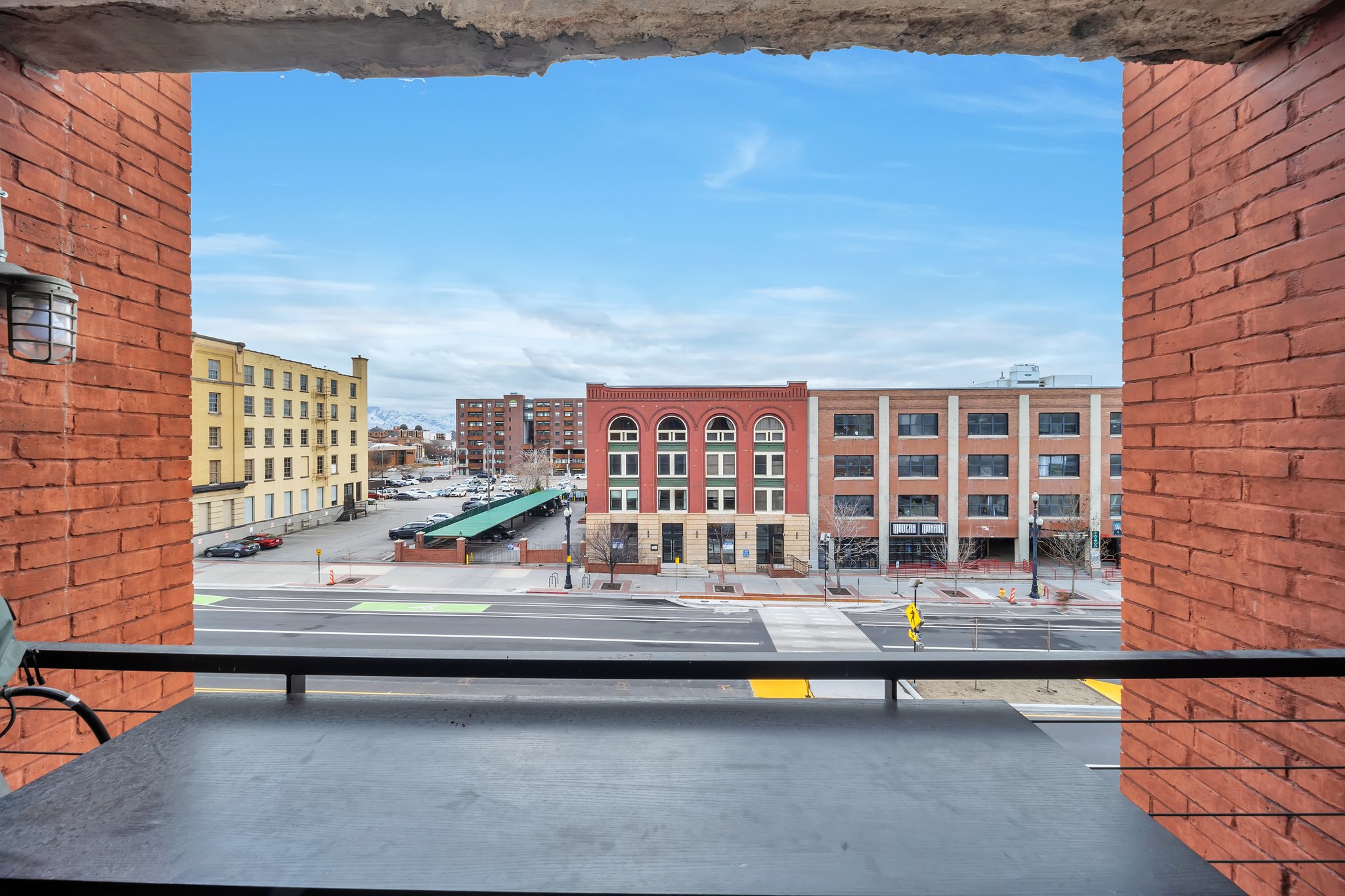 Balcony overlooking an urban streetscape with distinct brick buildings and a covered parking area