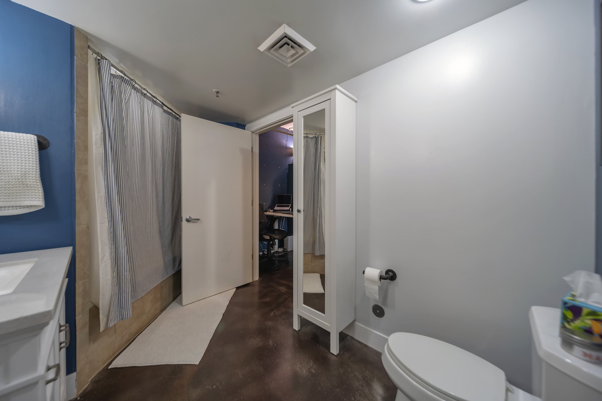 Bathroom featuring a shower with a striped curtain, a white vanity with an integrated sink, dark wood-finish flooring, a toilet, and a white storage cabinet with a mirrored door
