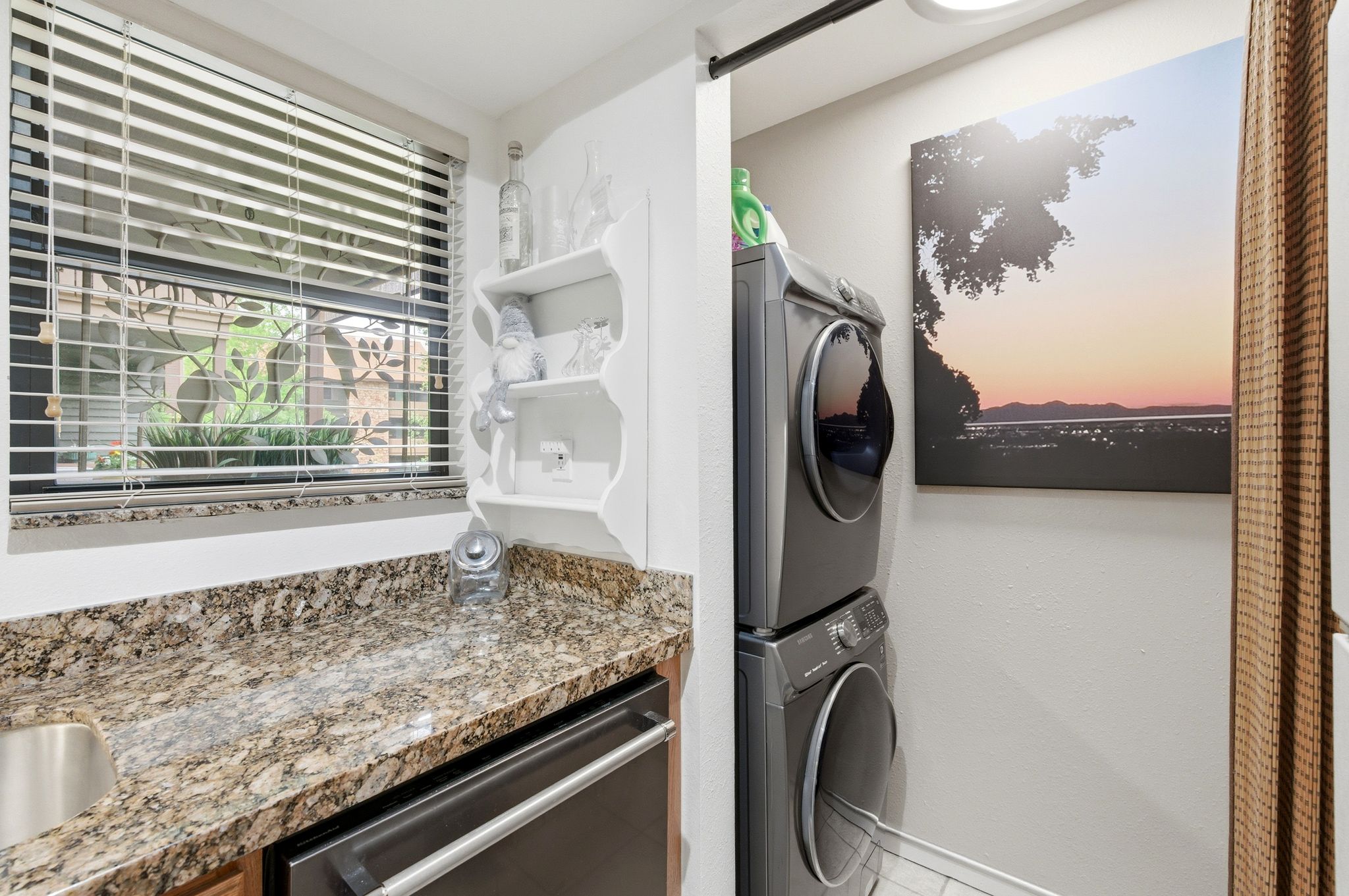 Laundry area featuring a stacked washer and dryer, granite-style countertop, undermount sink, and a built-in shelf
