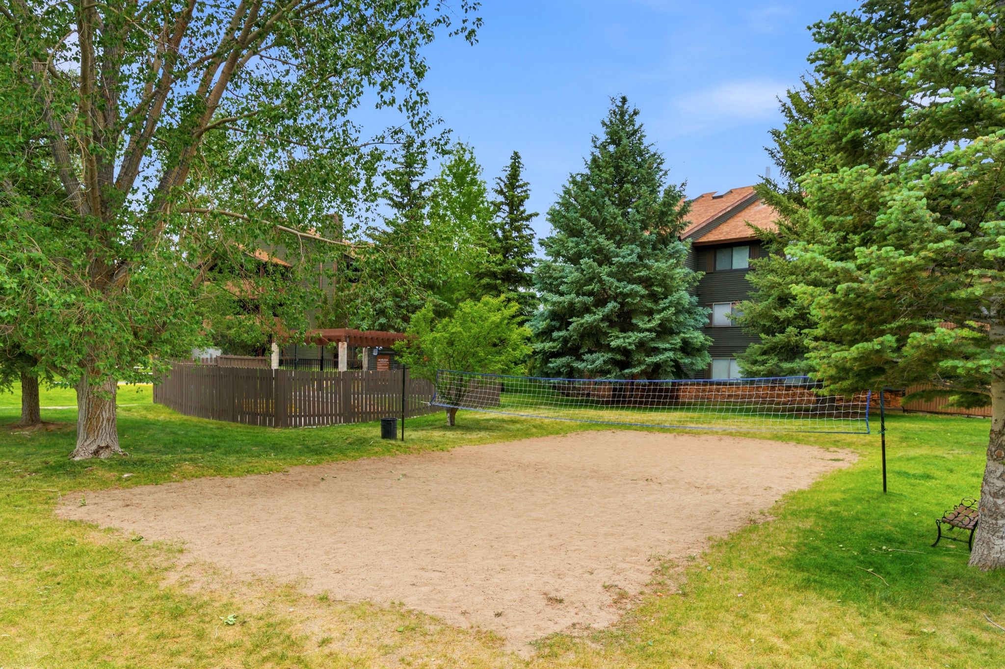 Sand volleyball court with a net, surrounded by mature trees and verdant lawns