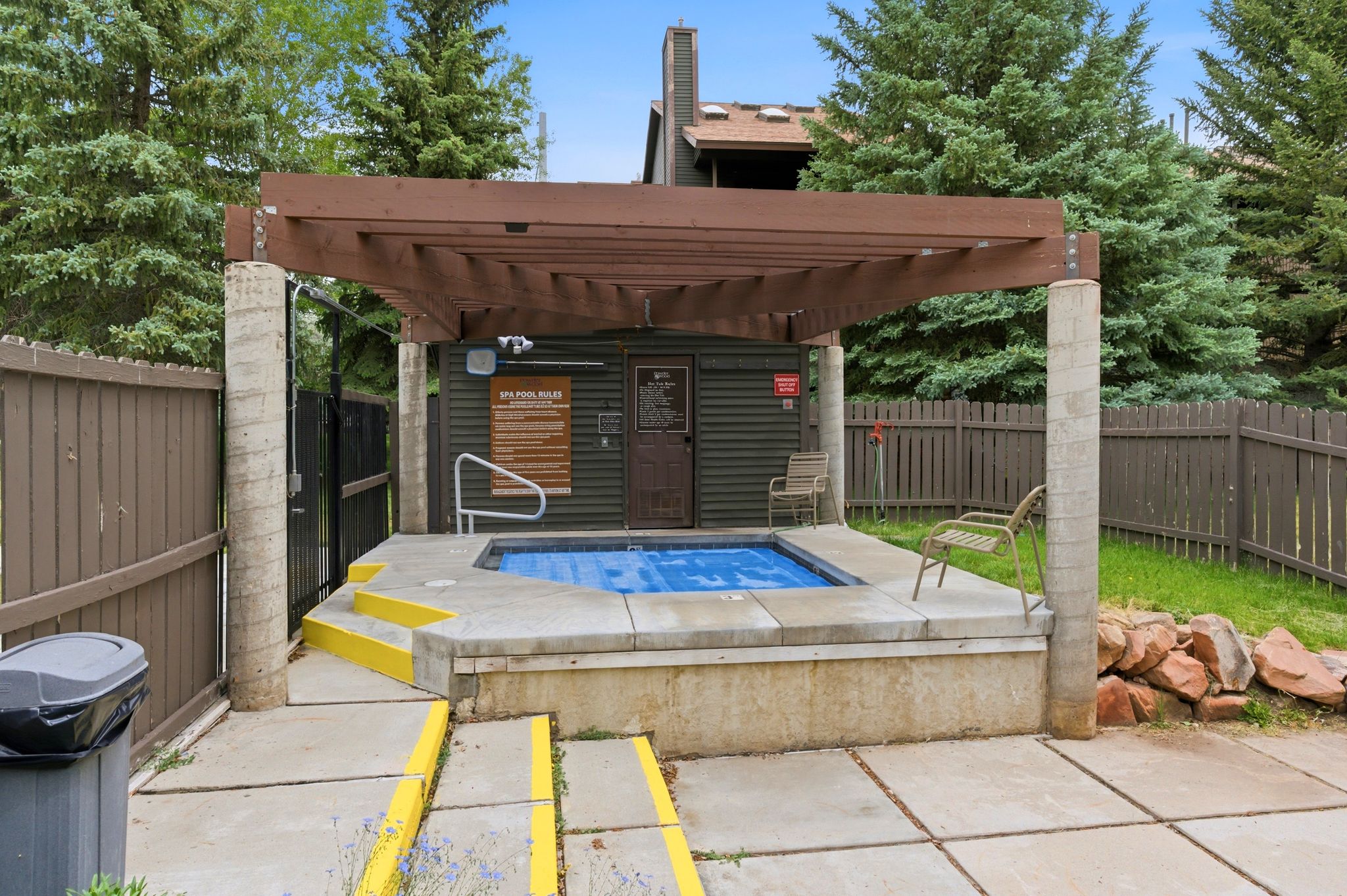 Outdoor spa with a slatted wooden pergola, concrete surround, and privacy fencing