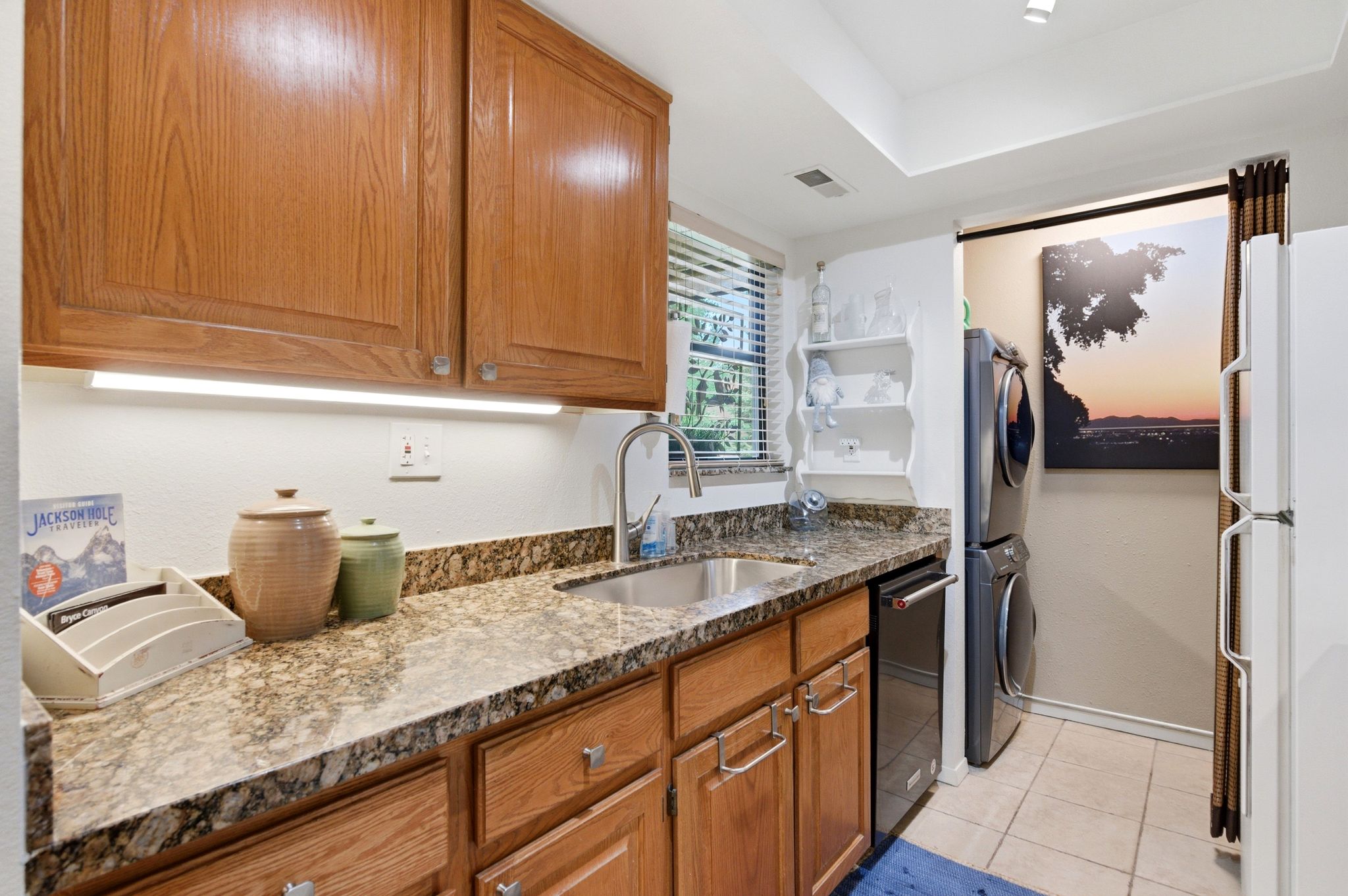 Kitchen area featuring wood-finish cabinetry, granite-style countertops, an undermount sink, and a window with blinds