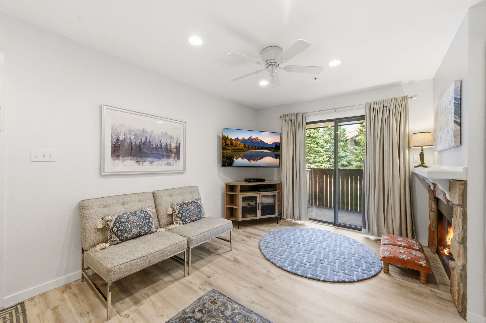 Living area featuring wood-finish flooring, a stone-clad fireplace with a mantel, a ceiling fan with integrated lighting, recessed lighting, and sliding glass doors opening to an exterior balcony