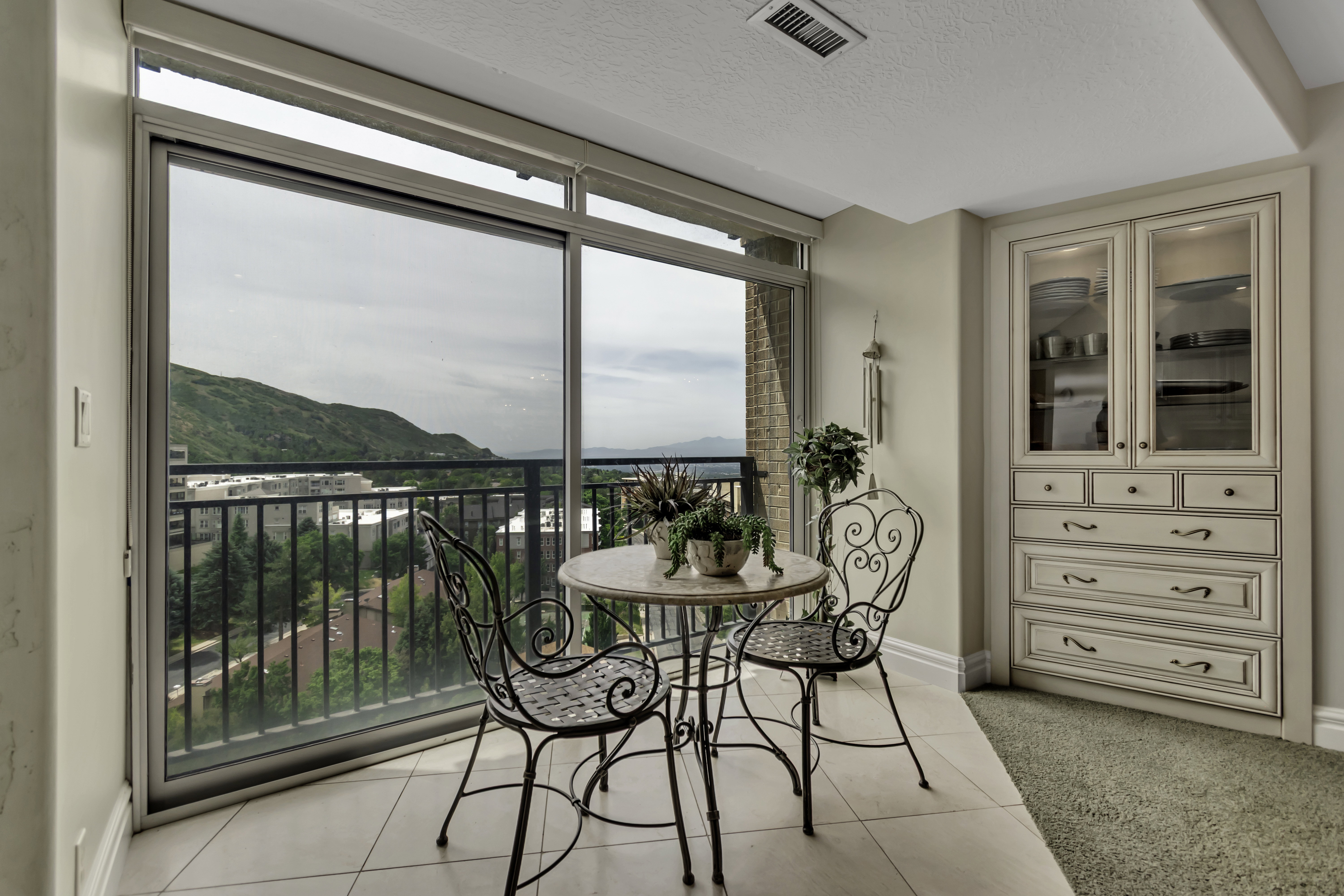 Sliding glass doors opening to a balcony with metal railing, featuring tile flooring and built-in cabinetry with glass display doors and lower drawers