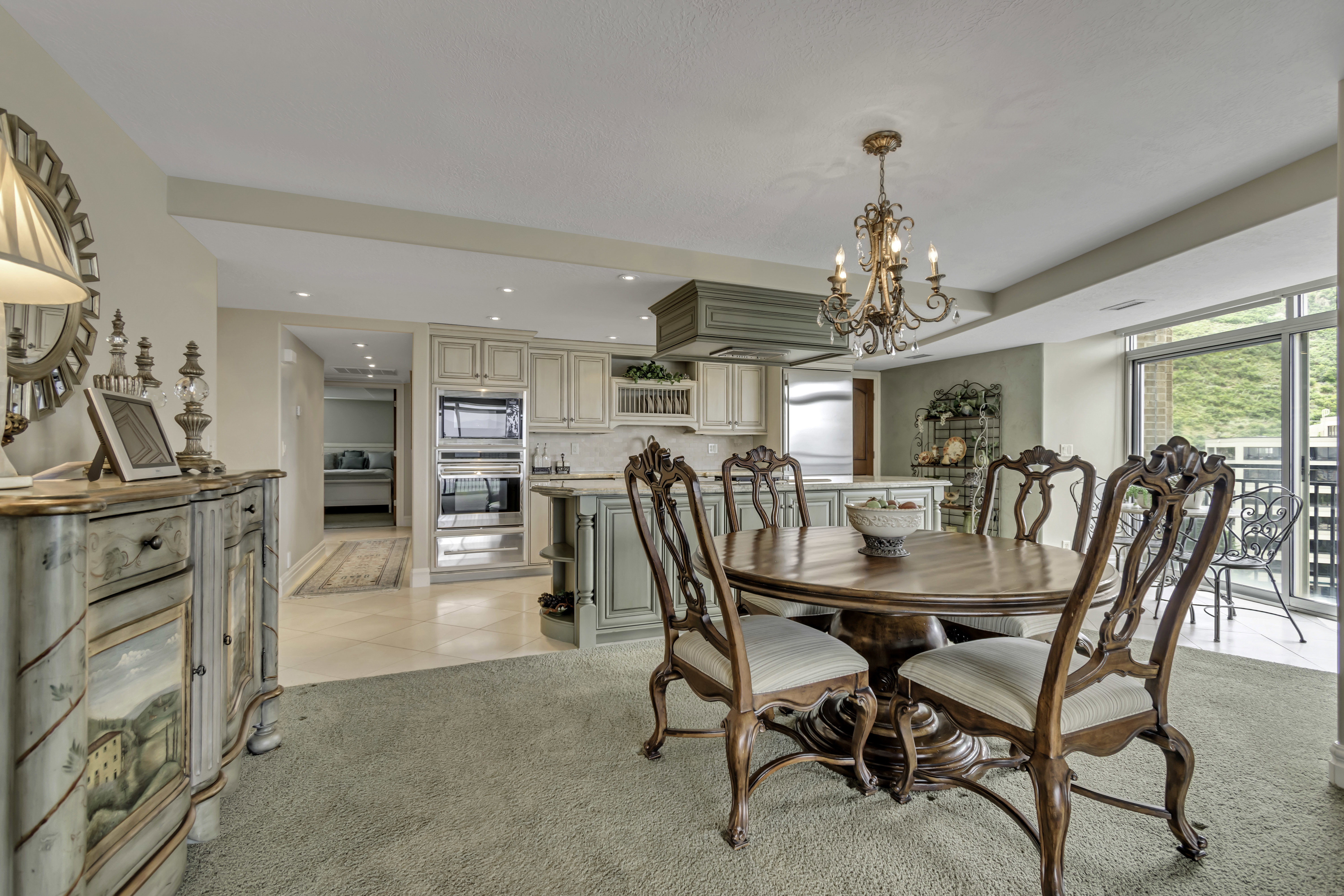 Spacious interior featuring a dining area with a chandelier, a kitchen with built-in appliances, and a balcony with a mountain backdrop