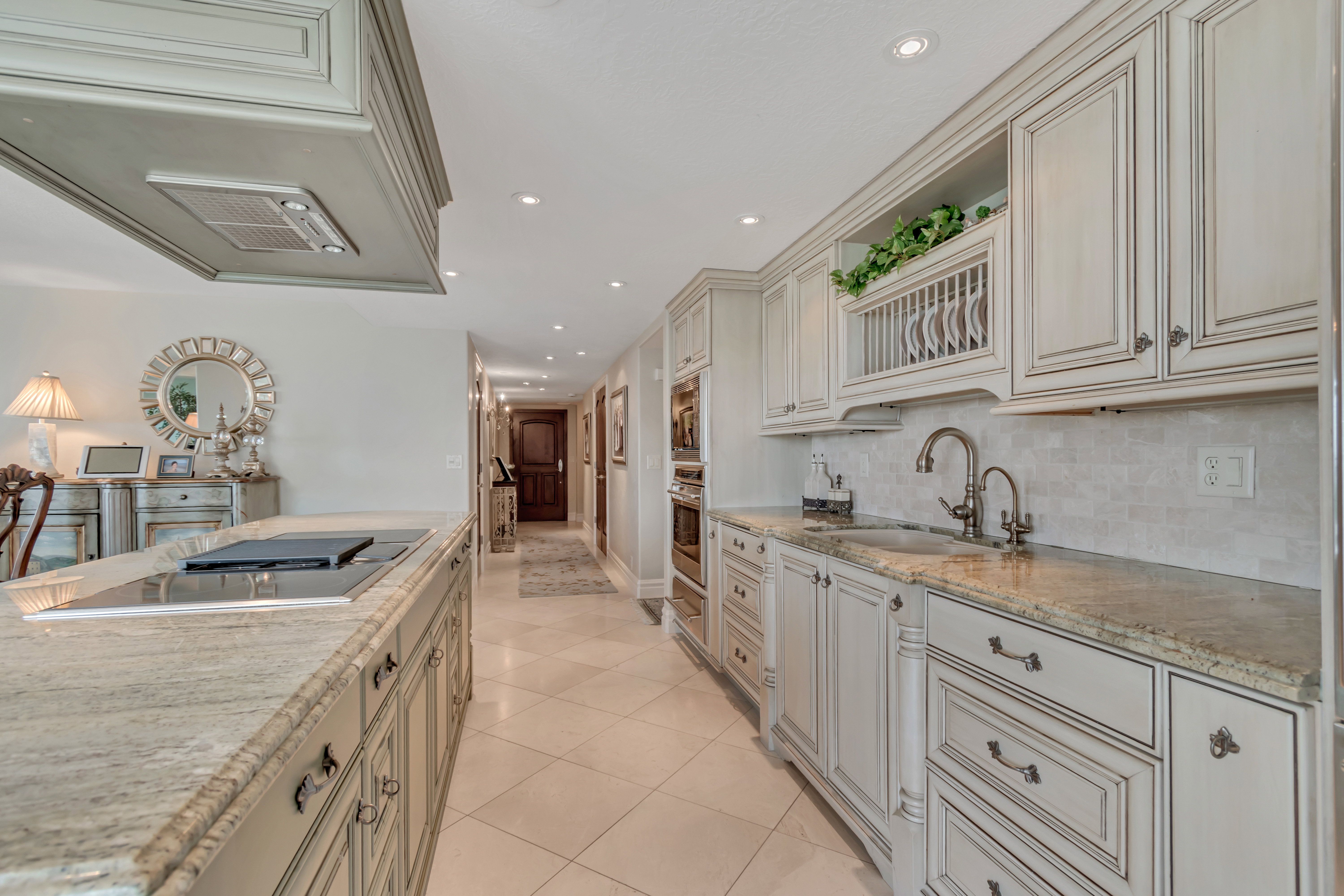 Gourmet kitchen featuring extensive cabinetry with decorative trim, granite countertops, an undermount sink with a gooseneck faucet, a built-in cooktop, and an integrated oven