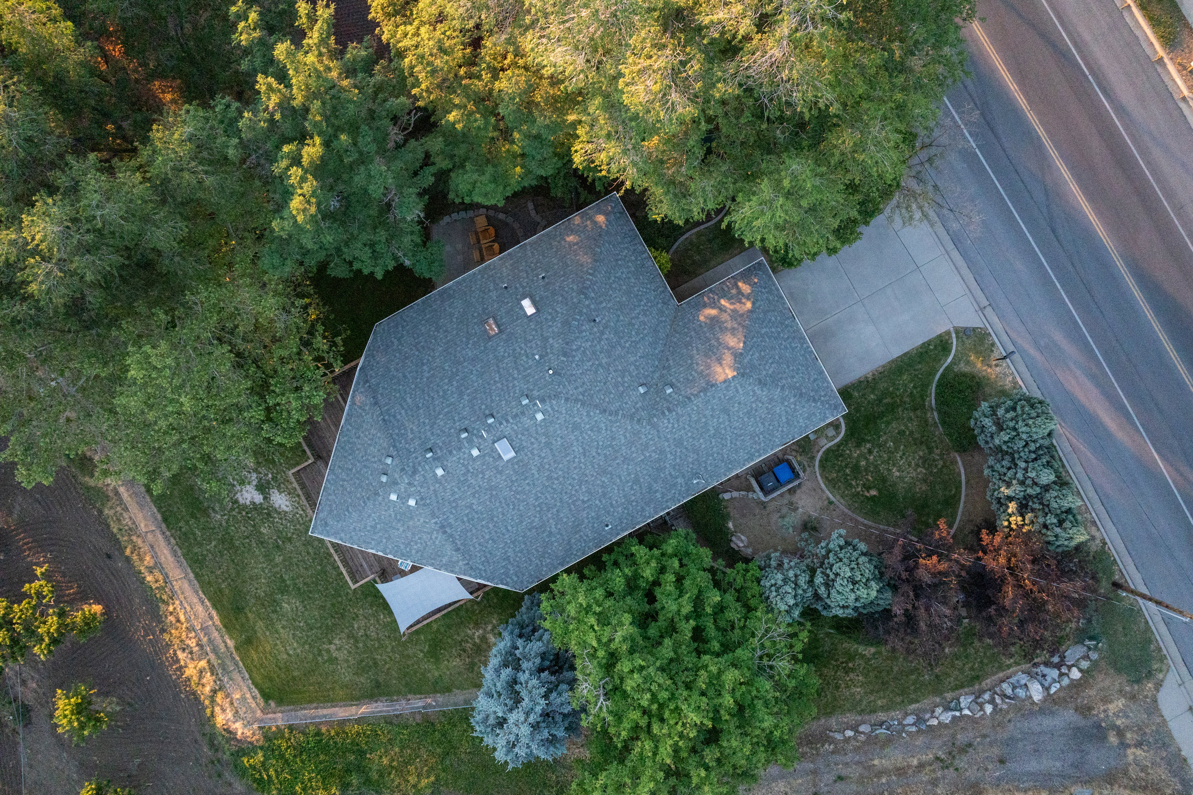 Aerial view showcasing the property's main residence with a gray shingle roof, surrounded by mature trees