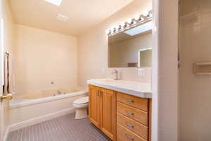 Bathroom featuring a built-in tub, skylights, wood-finish vanity with a single basin sink, and a tiled shower stall