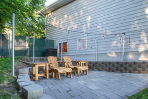 Paved patio area with string lighting, bordered by a concrete block retaining wall and a chain-link fence