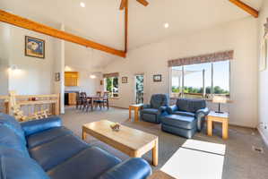 Vaulted ceilings with exposed wood beams, expansive windows, recessed lighting, and a neutral carpeted floor