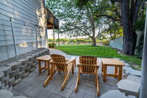 Paver patio with a stacked block retaining wall, manicured lawn, and mature trees